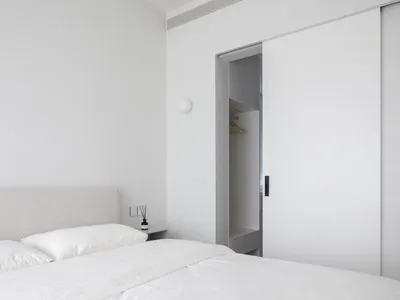A minimalist bedroom with a bed, white bedding, and a closed closet.