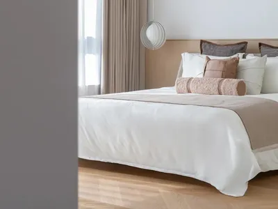 Modern minimalist bedroom with neutral-toned bedding, pillows, and curtains.
