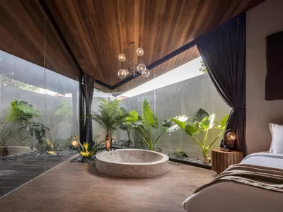 A minimalist bedroom featuring wooden elements and a circular stone bathtub surrounded by plants.