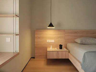 A minimalist bedroom with a wooden bed, floating nightstand, and floating shelves.