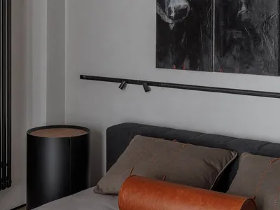 Modern bedroom with a gray bed, leather cylindrical pillow, and cushions, featuring abstract paintings of cows on the wall.