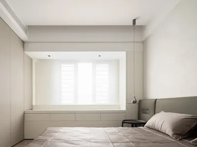 Neutral minimalist bedroom featuring a bed with a simple grey headboard, a window with white shutters, and built-in storage u