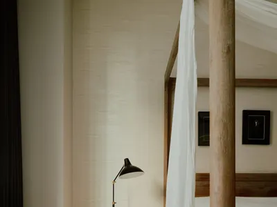 A minimalist bedroom featuring a wooden four-poster bed with a marble base and draped white curtains, alongside a side table