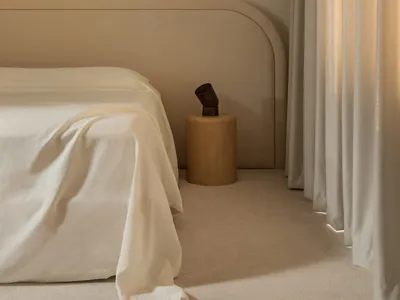 A minimalist bedroom featuring a bed with a textured cotton blanket, neutral-colored curtains, and a simple side table with a