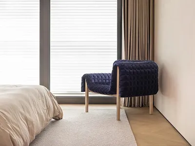 Minimalist bedroom with a textured blue armchair, white blinds, and wooden flooring.