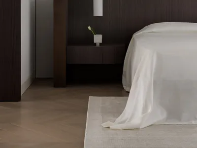 A minimalist bedroom with wooden furniture and soft textiles, featuring a floating nightstand with a vase of tulips and a sle