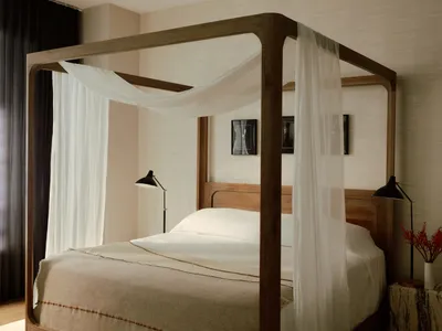 A minimalist bedroom with a wooden bed frame, white curtains, and black table lamps on either side of the bed.