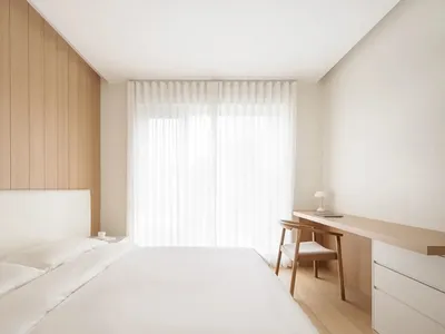 現代臥室搭配白色織品床具、木質床頭板，以及帶紗簾的大窗。