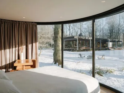 簡約臥室內擺放白色床鋪，玻璃窗外可見雪景，搭配現代家具。