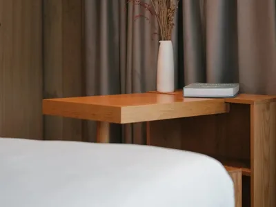 A minimalist bedroom featuring a wooden side table with a vase of dried flowers and a book.