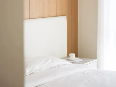 A minimalist bedroom featuring white furniture and wood paneling.