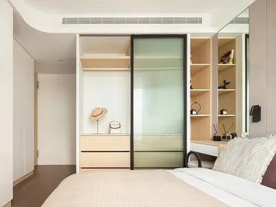 A minimalistic bedroom with neutral tones, featuring a bed, wardrobe, and organized shelves.