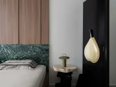 A minimalist bedroom featuring a bed with a marble headboard, wooden wall panels, and a black-framed artwork.