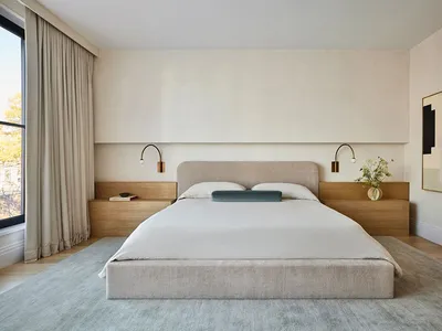 A minimalist bedroom with a neutral color palette featuring a bed with a fabric headboard, wooden nightstands, and brass wall