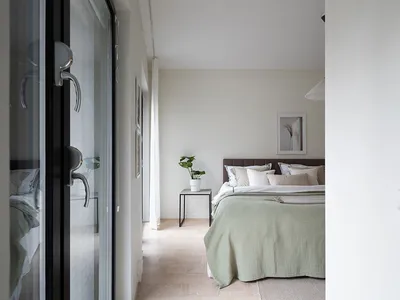 A minimalist bedroom featuring a bed with a muted green bedspread and a headboard, accompanied by neutral-toned bedding and a