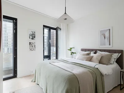 A modern bedroom with light-colored furniture and green bedding, featuring a large window with city views and a minimalist de