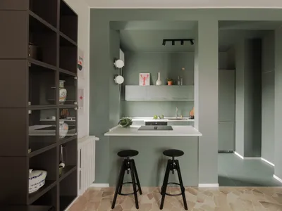 Minimalist kitchen with concrete surfaces, white countertops, and black stools.