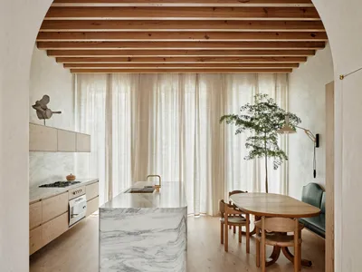 Modern residential kitchen featuring a marble countertop, wooden cabinets, and fabric curtains.