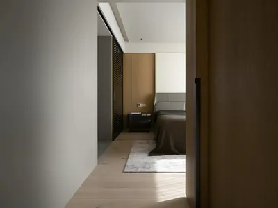 一間現代簡約臥室，搭配淺木地板、白地毯與灰色床鋪。