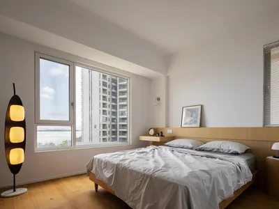 A minimalist bedroom featuring a wooden bed and a tall, multi-lamp floor lamp.