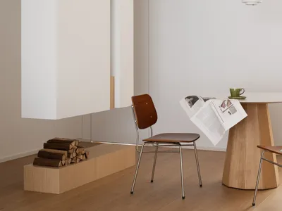 A minimalist living room with white walls, wooden furniture, and a metal pendant light hanging above a wooden dining table.