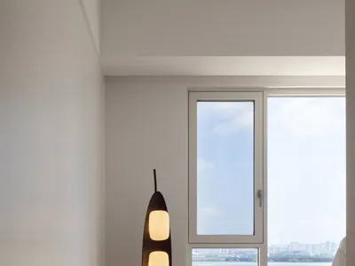 A modern minimalist bedroom with wooden flooring, a large window, and a floor lamp