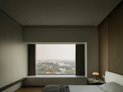 A modern bedroom with brown and neutral colors, featuring a large window showcasing a cityscape with a river and trees.