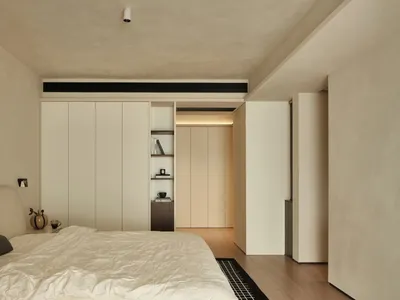 A minimalist bedroom with white and beige furniture and a simple, clean design.