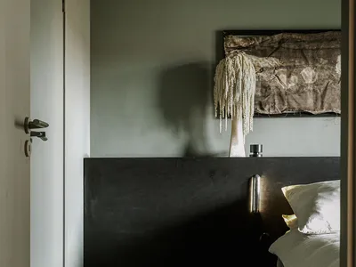 A minimalist bedroom with a black wooden headboard and a white bed, featuring a unique hanging lamp and a textured wall decor