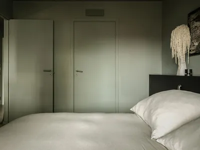 Minimalist bedroom with neutral tones, featuring a large bed, white pillows, and two green doors.