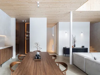 Modern living, dining, and kitchen area featuring wooden furniture and concrete walls.