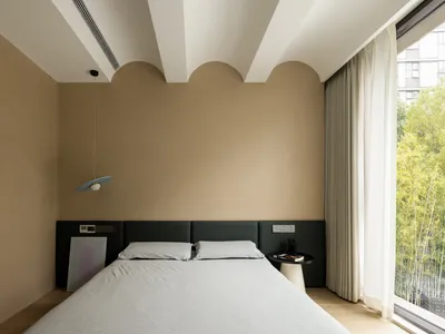 A minimalist bedroom with a white sheet on the bed, beige walls, and a hanging light fixture.