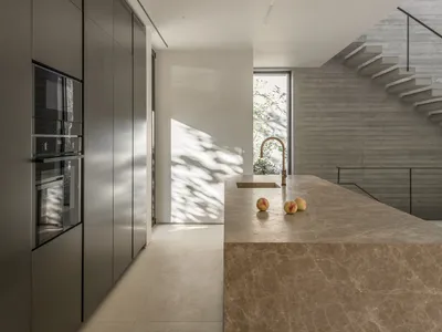 Modern minimalist kitchen with concrete countertop and floor, featuring sleek, integrated appliances and a central island wit