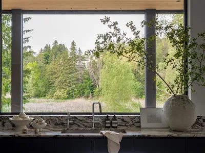 A modern kitchen with a marble countertop and sink overlooking a forested landscape.