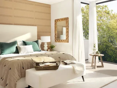 A minimalist bedroom featuring a bed with green and white pillows, a woven headboard, and a large window with sheer curtains,