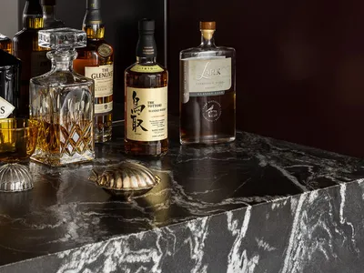 Modern bar counter made of marble with various bottles and glasses.