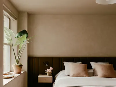 Modern bedroom featuring minimalist design with neutral textiles, a large window, and a cozy bed setup.