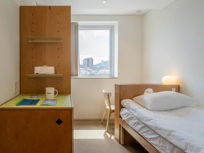 A minimalist bedroom featuring wooden furniture and a window with a view of a cityscape.