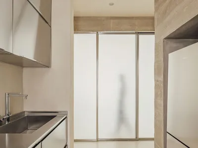 Modern kitchen with metallic cabinets and sink, frosted glass partition, and white flooring.