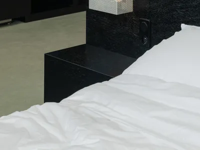 Modern minimalist bedroom featuring a textured black wooden platform bed with white bedding and a geometric lamp on the headb