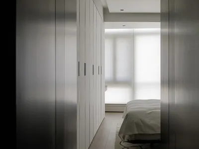 A modern minimalist bedroom with a wooden floor and a bed covered with white sheets.