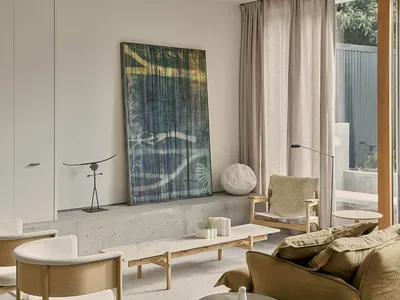 A minimalist living room with a concrete console table, wooden armchairs, and a large abstract artwork on the wall.