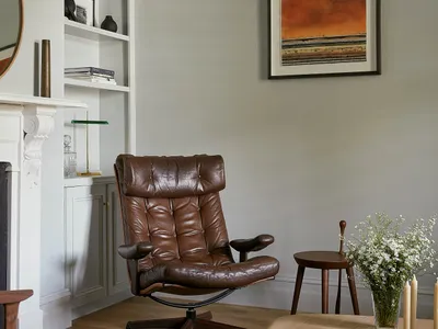 A minimalist living room featuring a brown leather reclining chair, a wooden coffee table, bookshelf, and framed artwork