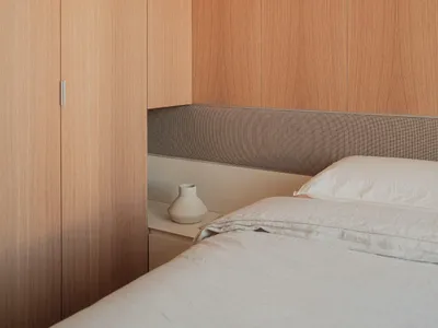 A bedroom with a minimalistic design featuring a monochrome color scheme and a wooden cabinet.