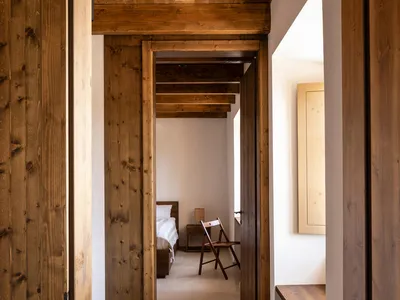 A minimalistic bedroom with wooden walls and ceiling beams, featuring a single bed and a small table.