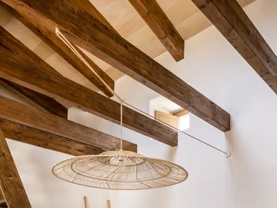 Minimalist bedroom featuring wood beams, wicker chandelier, and fabric bedding.