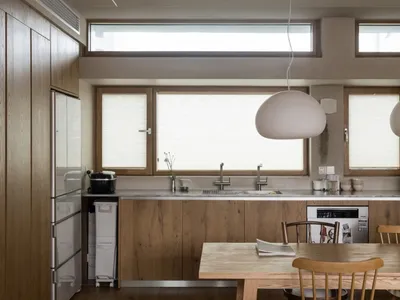 A minimalist residential kitchen featuring wood and stainless steel elements, with ample natural light through large windows.