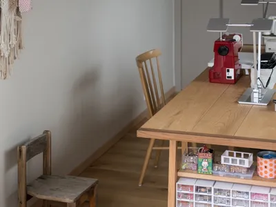 A wooden table with a sewing machine and various materials in a home office/craft room setting.
