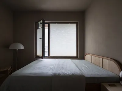 A minimalist bedroom with a fabric bed and a window with blinds.