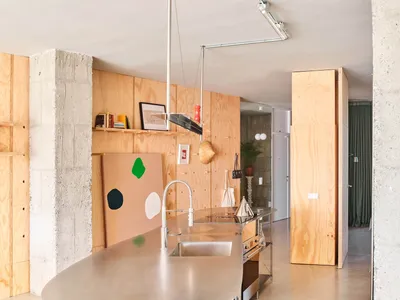 A modern minimalist kitchen with concrete walls and a stainless steel counter.